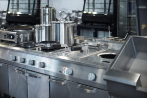 Three stainless steel pots and one pan are sitting on burners in an all-stainless steel industrial kitchen